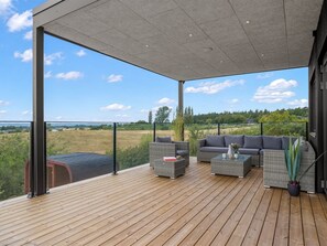 A covered outdoor deck with a wooden floor, grey wicker furniture, and a view of a green landscape. - "Hubertina" - 900m from the sea by Interhome (Ebeltoft)
