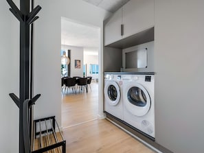 A modern laundry room with two front-loading washing machines, a microwave above, and a dining area in the background. - "Hubertina" - 900m from the sea by Interhome (Ebeltoft)