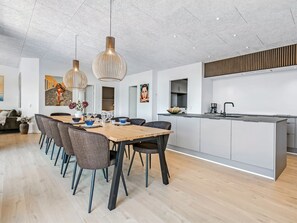 A modern kitchen with a central island, a dining area with a wooden table and chairs, and pendant lighting. - "Hubertina" - 900m from the sea by Interhome (Ebeltoft)