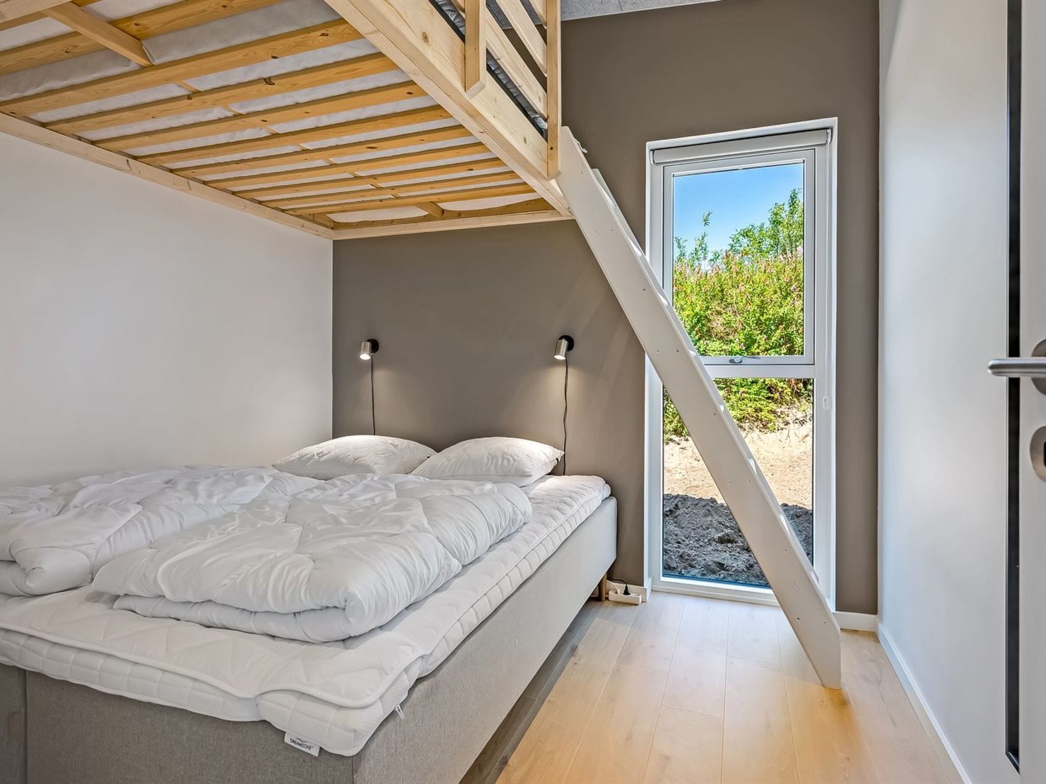 Una camera da letto con un letto, due lampade da comodino, una finestra con vista sul verde e un soffitto a spiovente.