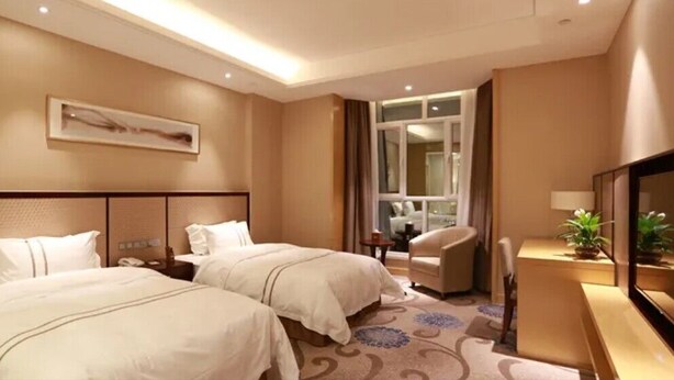 A hotel room with two beds, a desk, a chair, and a large window.