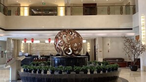 A spacious lobby with a central water feature, a decorative sphere, and potted plants.
