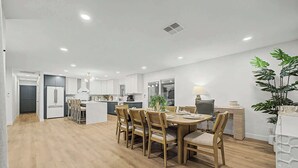 A modern kitchen with white cabinets, a central island, and a dining area with wooden chairs. - NEW Ocotillo Luxe Retreat Scottsdale Old Town (Scottsdale)