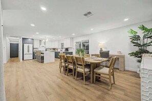 A modern kitchen with white cabinets, a central island, and a dining area with wooden chairs. - NEW Ocotillo Luxe Retreat Scottsdale Old Town (Scottsdale)