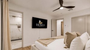 A modern hotel room with a bed, a television, a ceiling fan, and a bathroom with marble tiles. - NEW Ocotillo Luxe Retreat Scottsdale Old Town (Scottsdale)