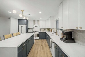 A modern kitchen with a central island, white cabinetry, and a coffee machine. - NEW Ocotillo Luxe Retreat Scottsdale Old Town (Scottsdale)