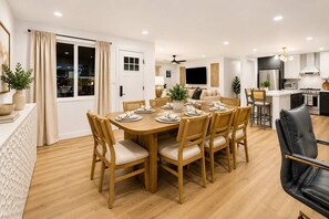 Un espace repas moderne avec une table ronde en bois, dressée pour six personnes, entourée de chaises en bois dotées d’assises rembourrées.