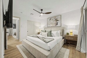 Une chambre à coucher moderne avec un lit, des tables de chevet, un ventilateur de plafond et un tableau au mur.