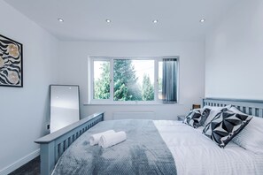 A bedroom with a bed, a window with curtains, a radiator, and a wall-mounted mirror. - Modern Chorlton Home | Parking | City and Airport (Manchester)