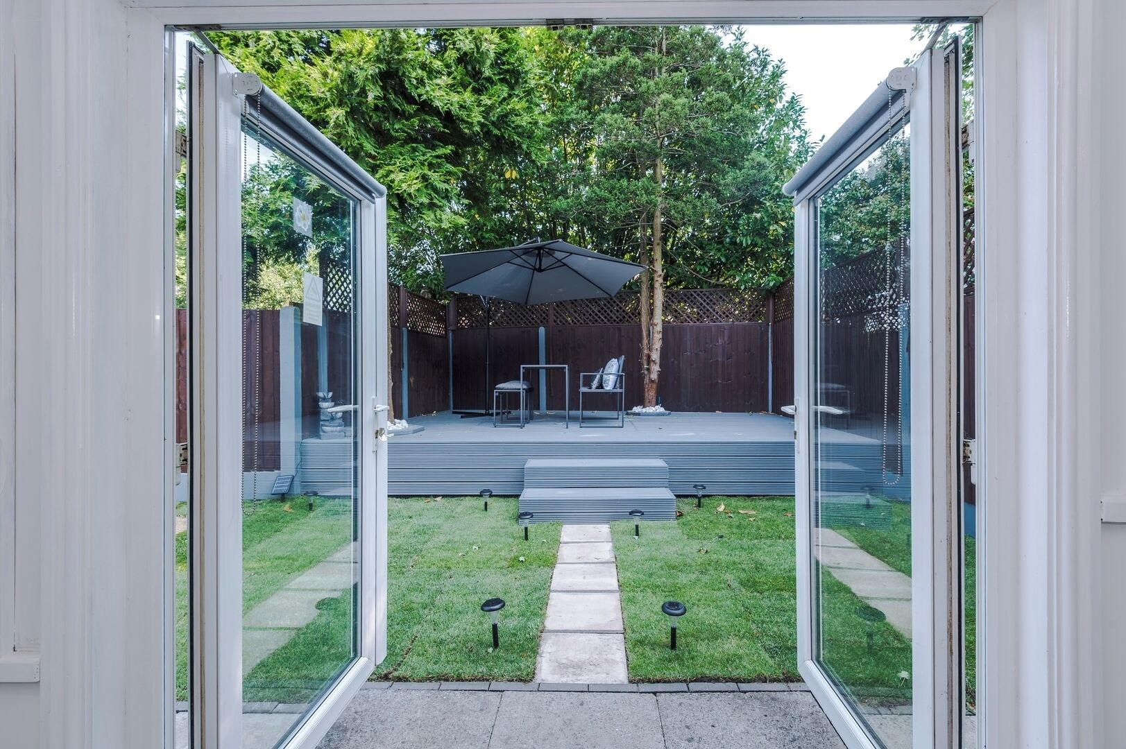 Une porte vitrée donne accès à un patio situé dans le jardin, où se trouvent une table, des chaises et un espace abrité.
