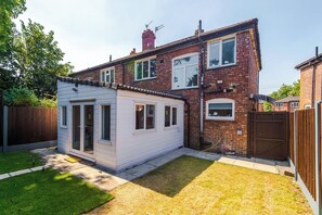 Ein zweistöckiges Haus mit einer kleinen angebauten Garage, einem eingezäunten Garten und einem Holzzaun.
