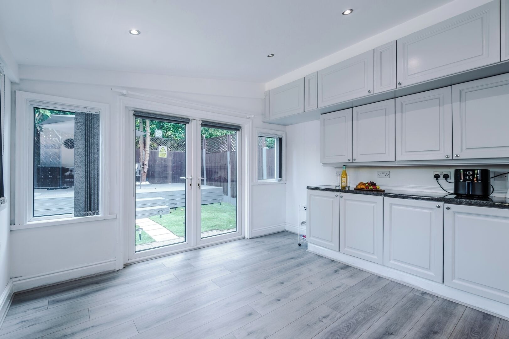A modern kitchen with white cabinetry, a black countertop, and a view of a backyard through glass doors.
