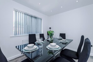 Ein moderner Essbereich mit einem Glastisch, schwarzen Stühlen und einem Fenster mit Jalousien.