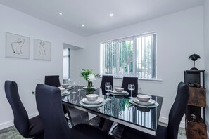 Un comedor moderno con una mesa de vidrio, sillas negras, platos blancos y un florero con flores.