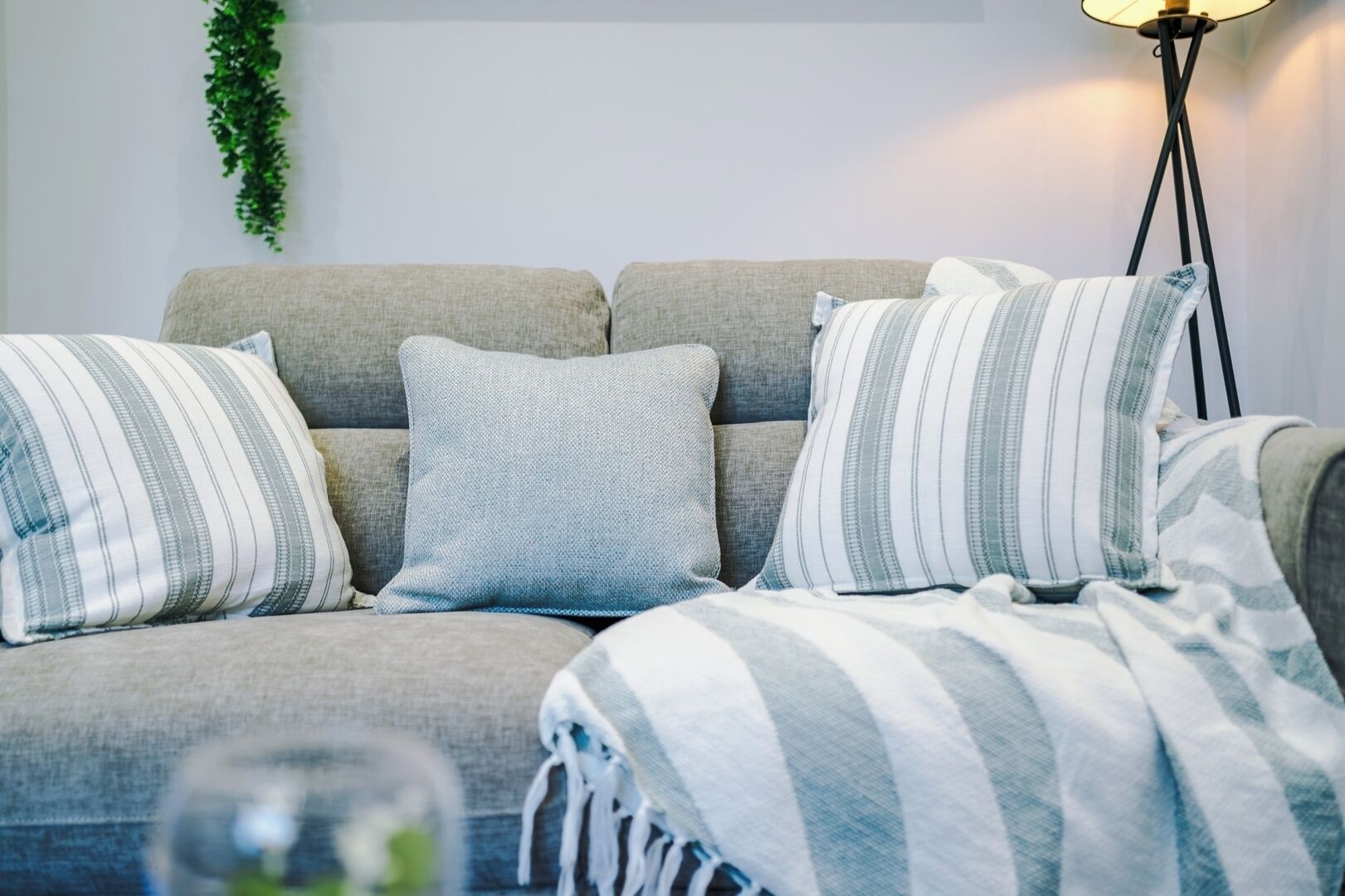 Ein Sofa mit gestreifteren Kissen und einer Decke, eine Stehlampe und eine Zimmerpflanze.
