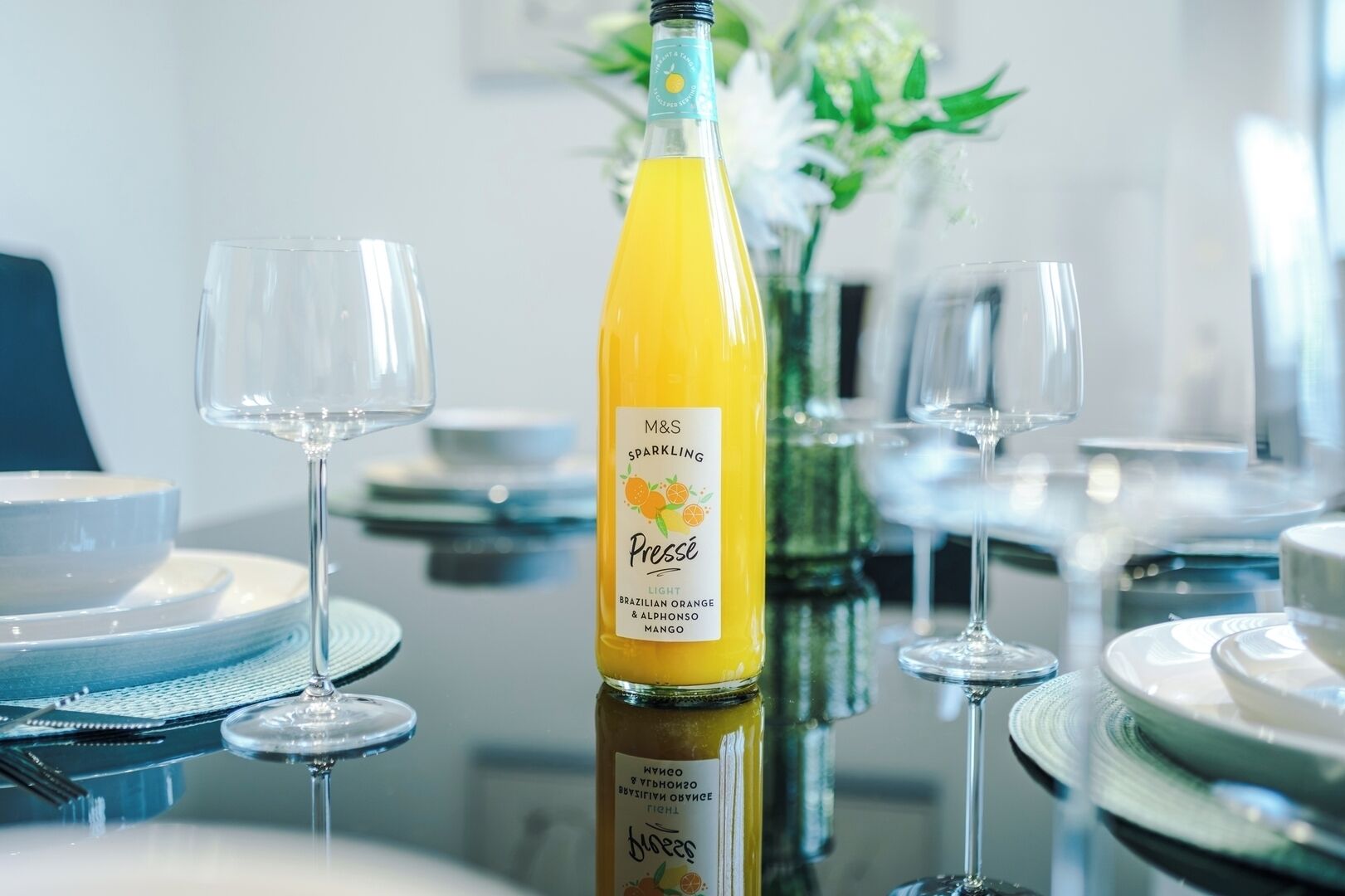 A dining table with a bottle of M&S Sparkling Presse, a glass, and a vase with flowers.