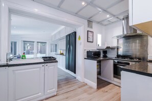 A modern kitchen with white cabinetry, a stainless steel range hood, and a microwave. - Modern Chorlton Home | Parking | City and Airport (Manchester)