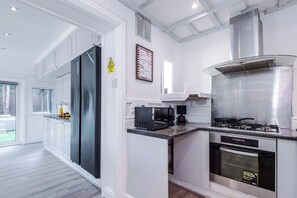 Una cocina moderna con armarios blancos, una campana extractora de acero inoxidable, horno empotrado y microondas.