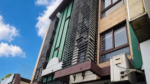 Un edificio a più piani con un design architettonico moderno, caratterizzato da una facciata verde e marrone ben definita, un condizionatore d'aria visibile e un'area di parcheggio con posti delimitati.