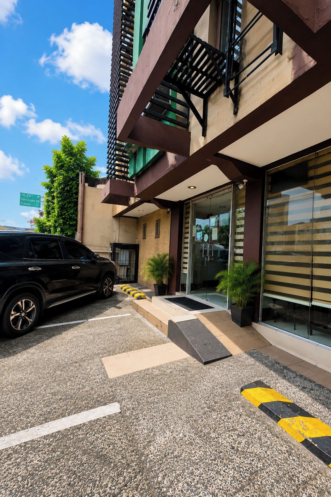 Un edificio moderno con un estacionamiento, una camioneta SUV negra y un cielo despejado.