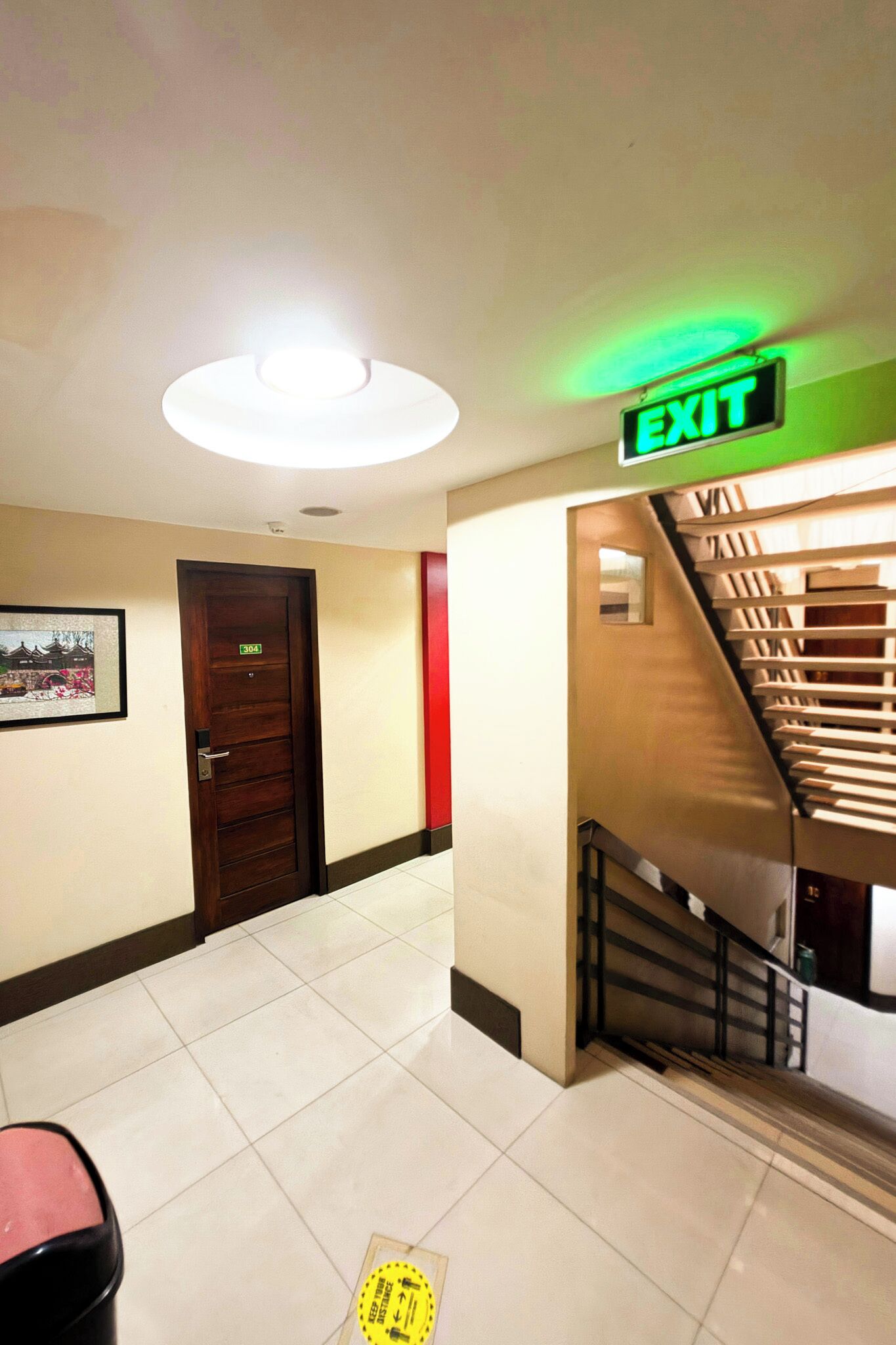 A hotel corridor with an exit sign, a door labeled '304', and a staircase.