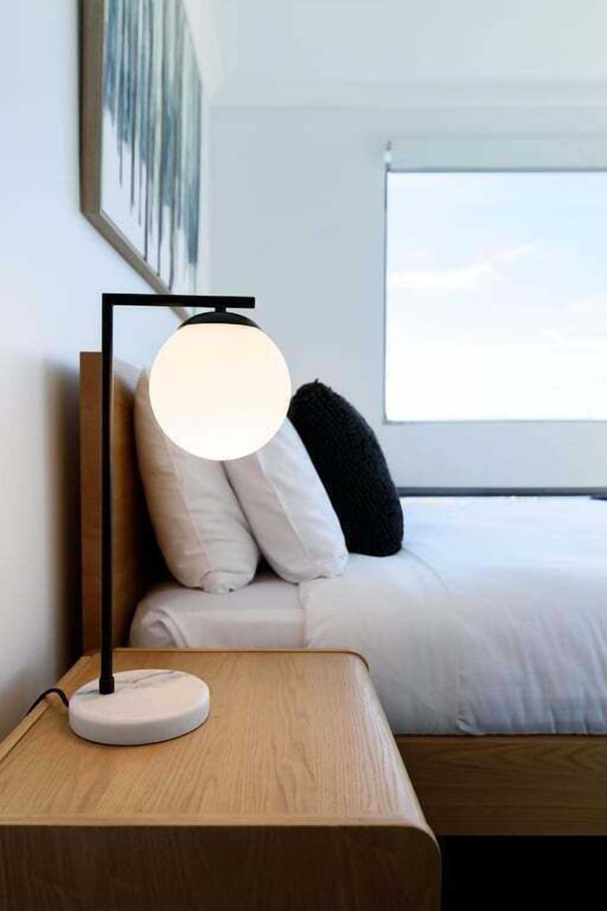A bed with white bedding, a black pillow, and a bedside table with a lamp.