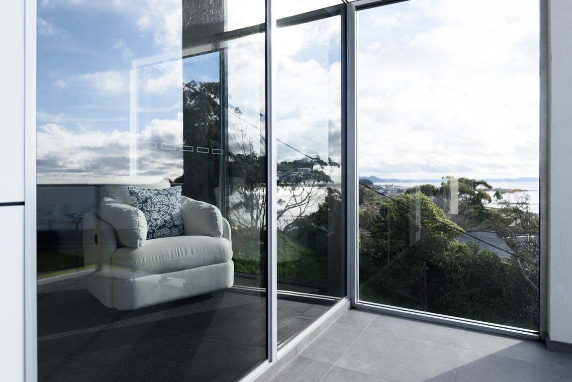 Une pièce moderne avec un grand mur de verre, un canapé blanc agrémenté de coussins à motifs et une vue sur un paysage urbain et des collines.