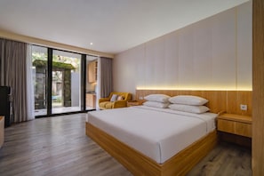 A modern hotel room with a large bed, a wooden nightstand, a yellow armchair, and a sliding glass door leading to an outdoor area. - Sunrise Suite Kerobokan (Bali)