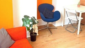 Une pièce avec une chaise bleue, un bureau blanc et une plante en pot.