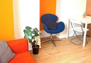 Ein Zimmer mit blauem Sessel, weißem Schreibtisch und einem Blumentopf.