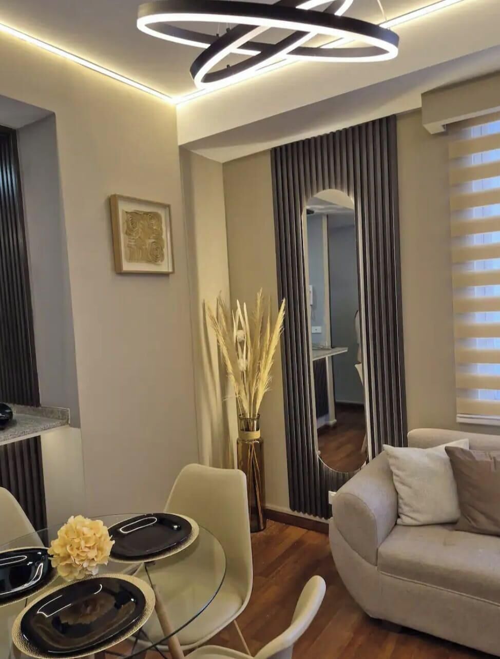 A modern living room with a glass dining table, a sofa, and a decorative vase with dried plants.