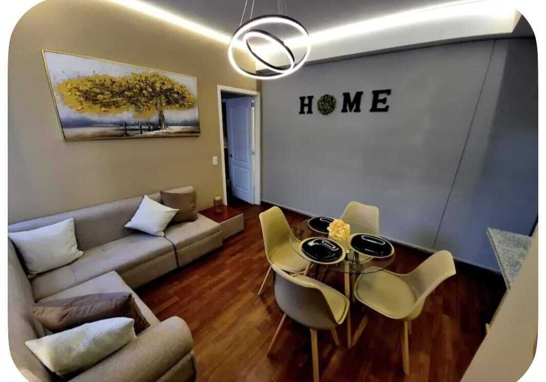 Un salon avec un canapé, une table à manger et des chaises, un tableau accroché au mur et une enseigne portant l’inscription « HOME ».