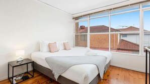Une chambre avec une grande fenêtre, un lit avec des oreillers, une table de chevet avec une lampe et un plancher en bois.