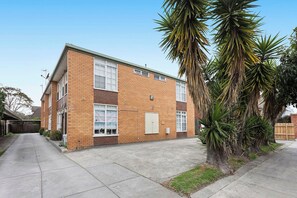 A two-story building with a brick facade, large windows, and a small courtyard with palm trees. - Domi Rentals - The Murra Apartment (Murrumbeena)