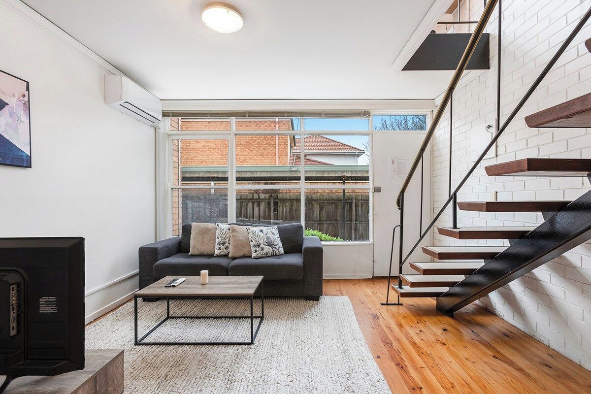 A modern living room with a sofa, coffee table, and a fireplace. There is a staircase with a black railing and wooden steps.