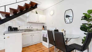 Une cuisine compacte avec des meubles blancs, un plancher en bois, une table à manger avec des chaises et un escalier avec des marches marron.