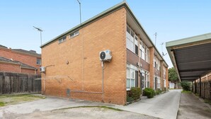 Un immeuble résidentiel de deux étages, doté d’une façade en briques, d’un espace de stationnement couvert et d’une antenne parabolique visible.