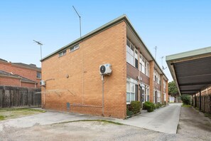 A two-story residential building with a brick facade, a covered parking area, and a visible satellite dish. - Domi Rentals - The Murra Apartment (Murrumbeena)