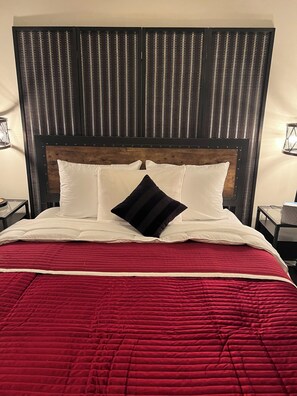 Un lit avec une couette rouge, des oreillers blancs et un coussin noir.
