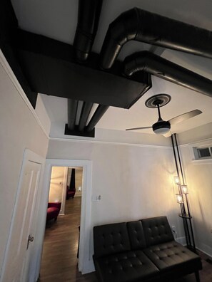 Une pièce dont les conduits de ventilation sont apparents, avec un ventilateur de plafond, un lit et un lampadaire.