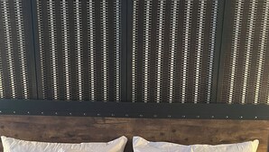 A bed with white bedding and a black pillow, set against a wooden headboard and a vertical striped background. - Historic Apt. Adjacent to Capitol/2 Queen Bds Loft Style near Medical/State Fair (Springfield)