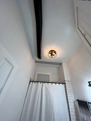 Une salle de bain avec un rideau de douche, un porte-serviettes et un luminaire au plafond.