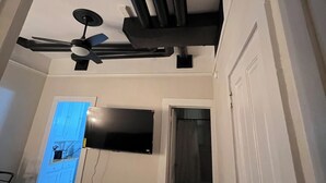 A room with a ceiling fan, a flat-screen TV mounted on the wall, a door, and a bag on the floor. - Historic Apt. Adjacent to Capitol/2 Queen Bds Loft Style near Medical/State Fair (Springfield)