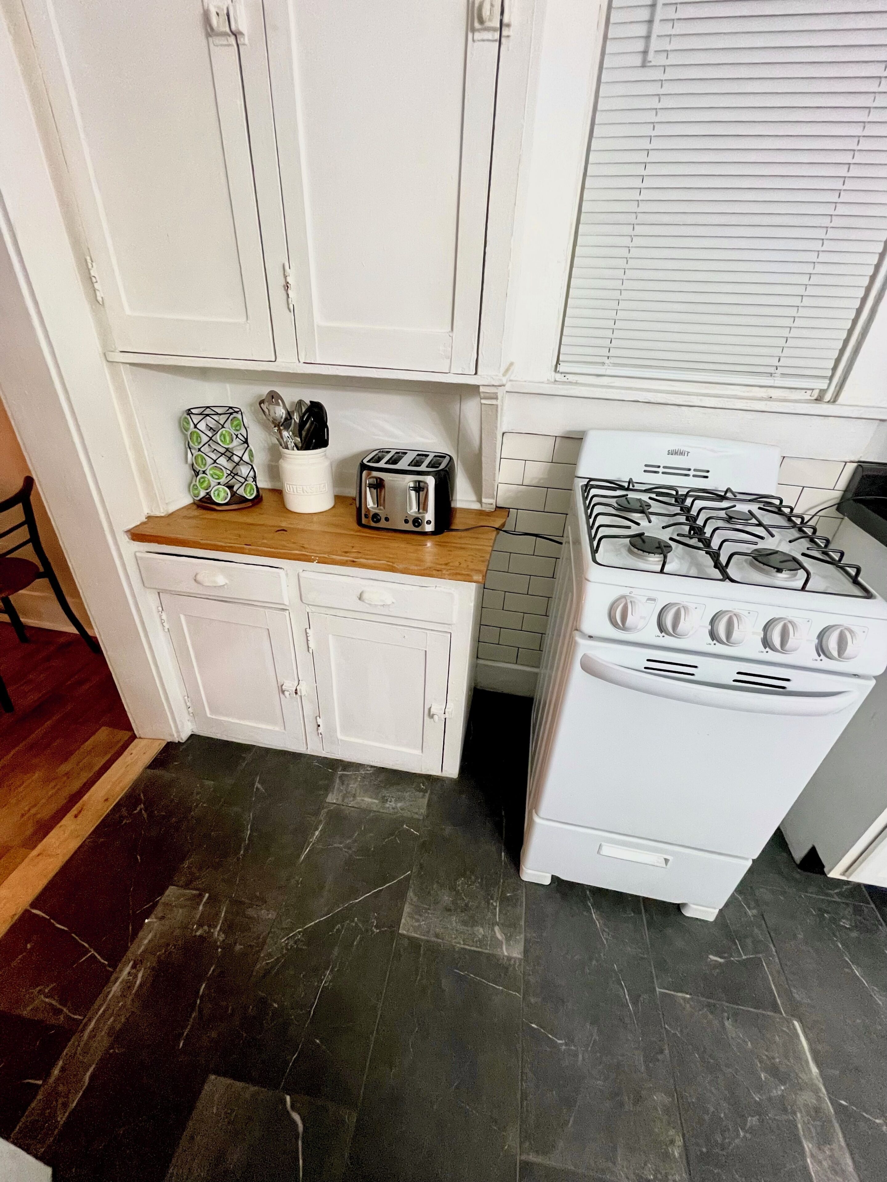 A kitchen with white cabinets, a wooden countertop, a toaster, a gas stove, and a tiled backsplash.