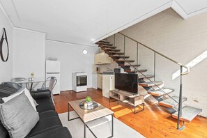 Un apartamento moderno con una escalera, una sala de estar con sofá y mesa de centro, un área de cocina y una mesa de comedor.