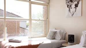 Une chambre avec deux lits, une grande fenêtre, un radiateur et une œuvre d’art accrochée au mur.