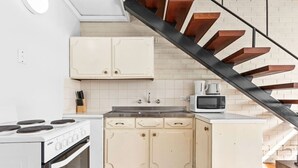 Une cuisine de taille réduite avec des meubles blancs, une cuisinière et un four à micro-ondes.