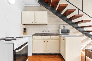 A compact kitchen with white cabinets, a stove, and a microwave. - Domi Rentals - The Murra Apartments (Murrumbeena)