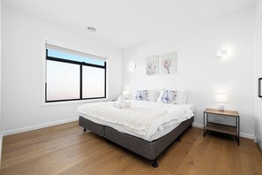 A bedroom with a large bed, a bedside table, a window, and wall-mounted lights.