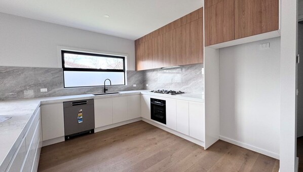 A modern kitchen with white cabinetry, a built-in oven, and a window above the sink.